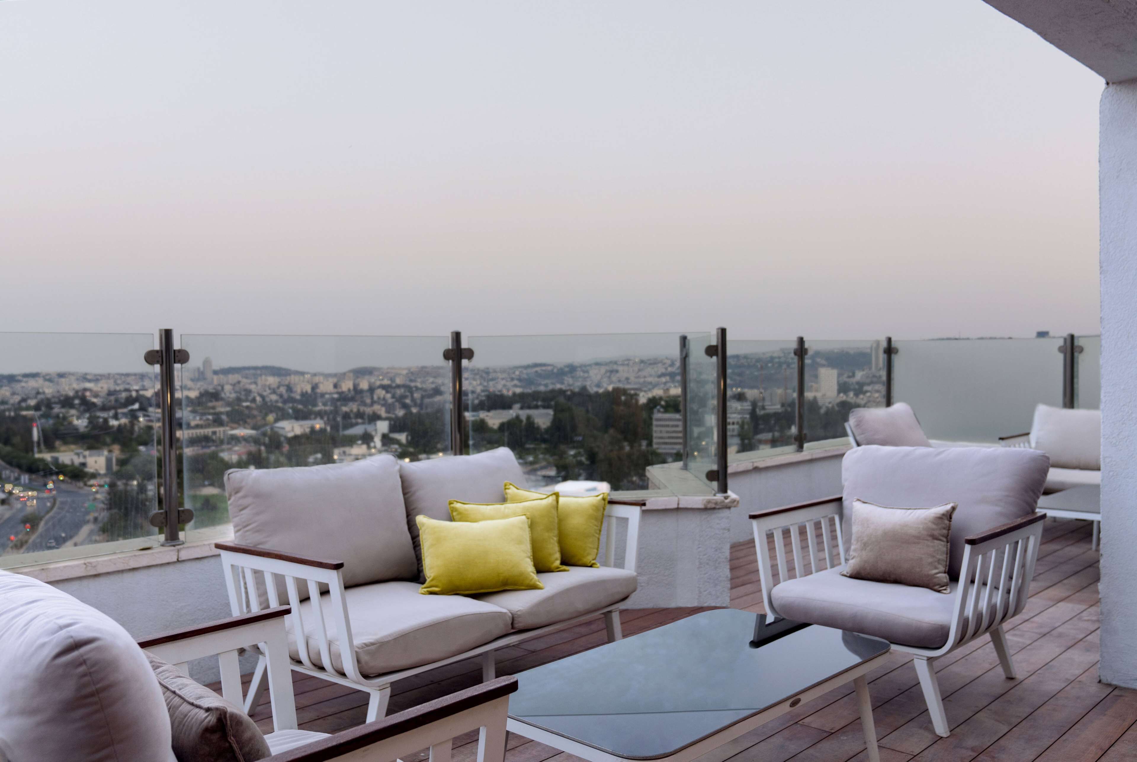 Ein Balkon mit einer Couch und Sesseln, mit Blick auf eine Stadtlandschaft.