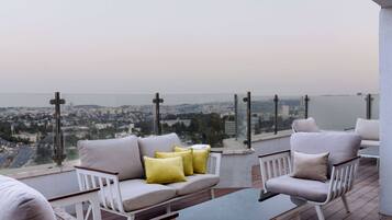 A balcony with a sofa and armchairs, overlooking a cityscape.