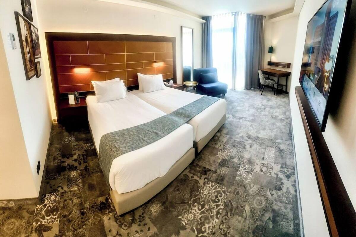 Quarto de hotel com cama de casal, escrivaninha, cadeira e televisão.