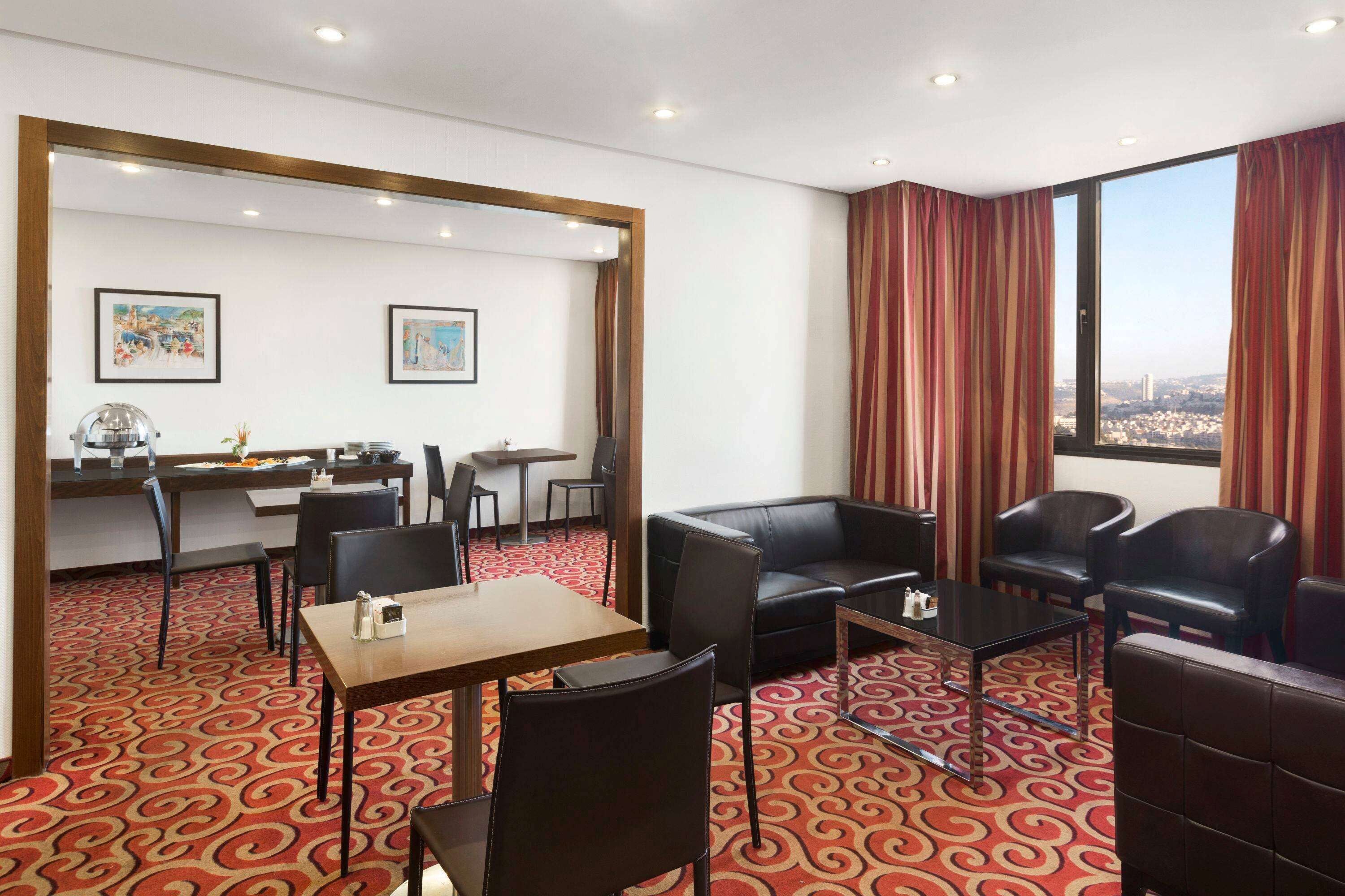 A hotel room with a dining area, a sofa, and a large window with curtains.