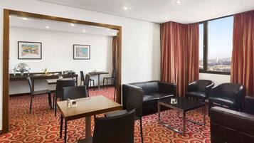 A hotel room with a dining area, a sofa, and a large window with curtains.