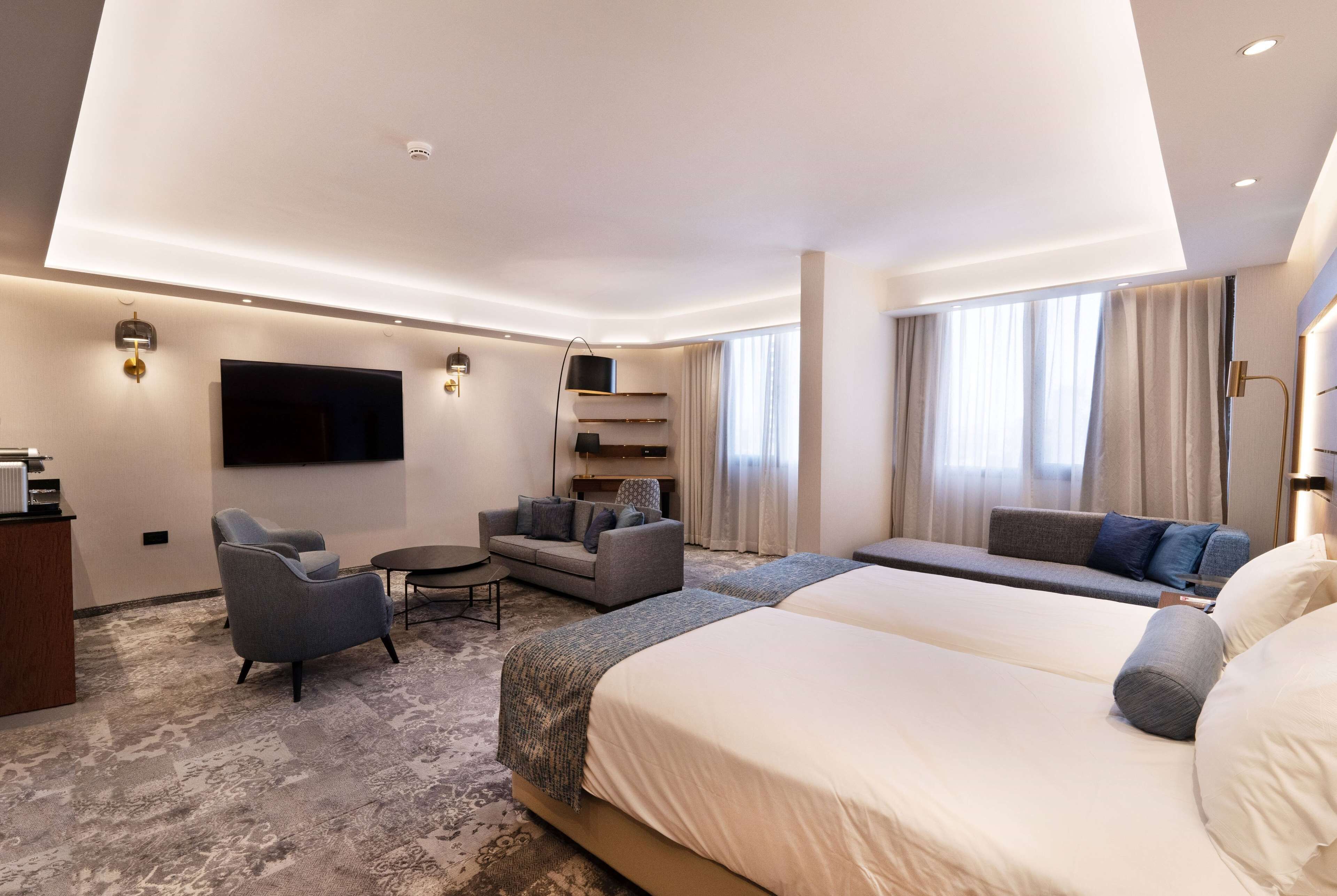 A modern hotel room with a large bed, a sofa, a desk, and a TV.