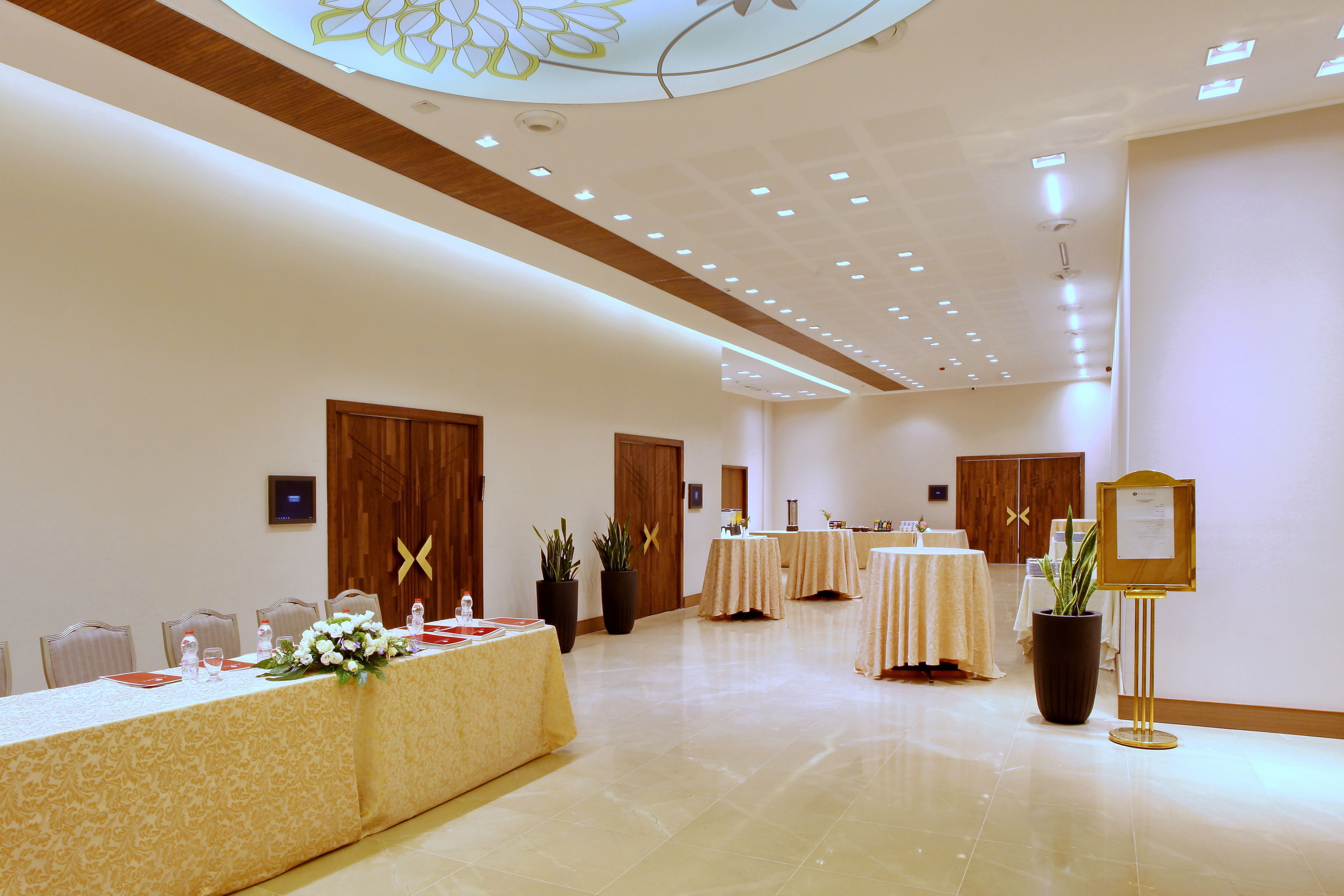 A conference room with a long table set for a meeting, surrounded by chairs, with potted plants and a bulletin board.