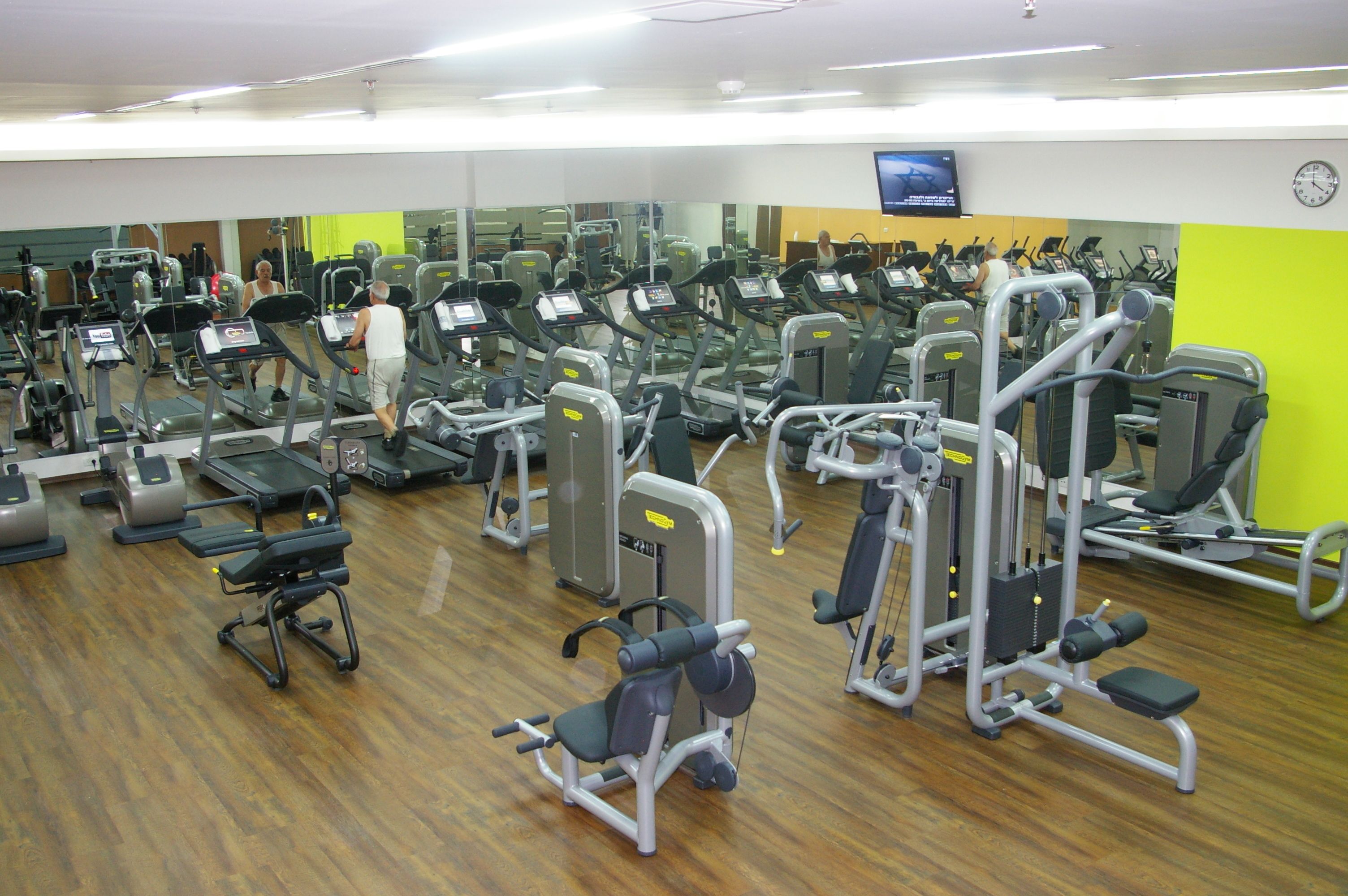 A gym with various exercise machines, mirrors, and a TV screen.