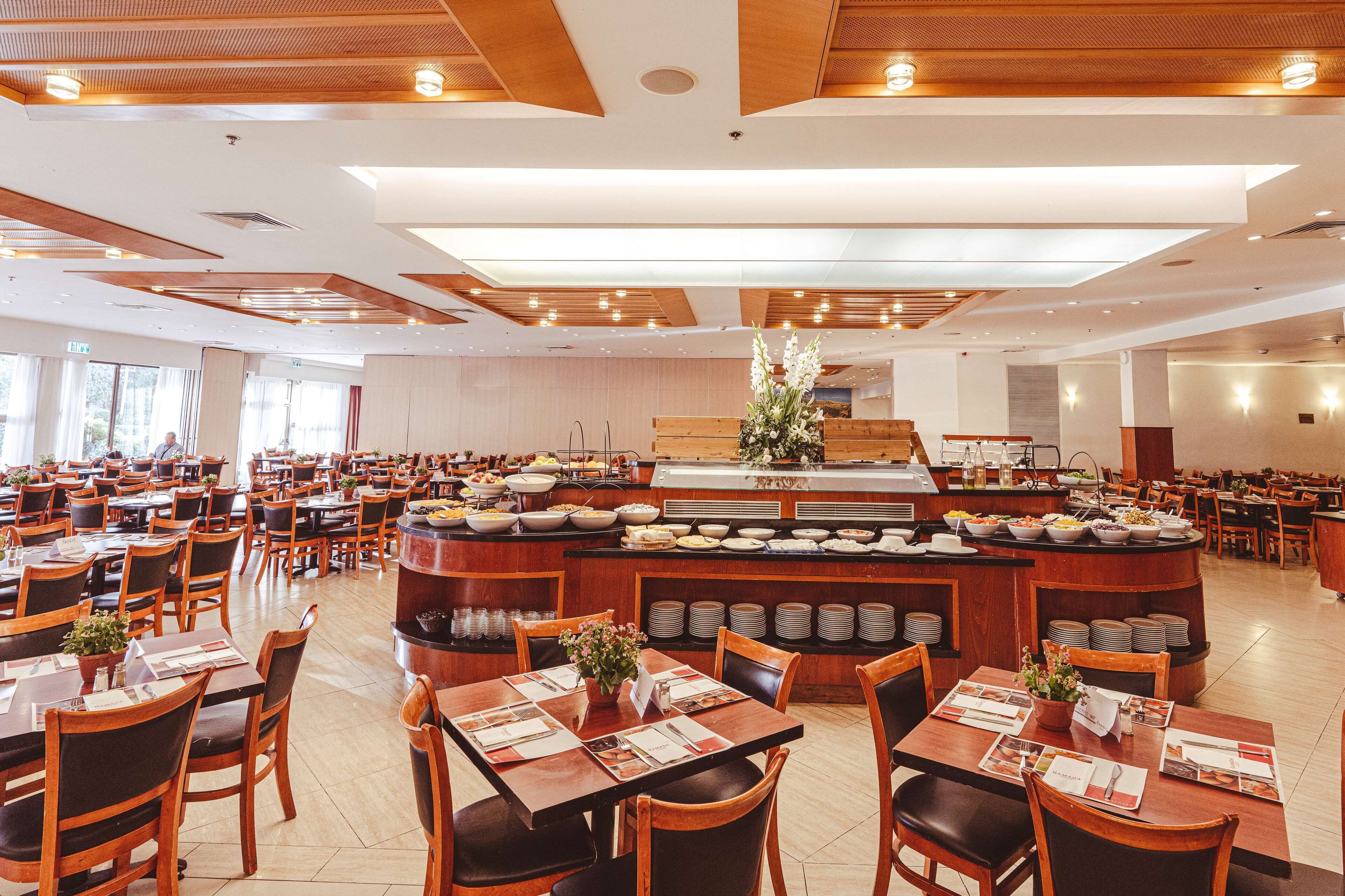 Een ruime eetruimte met meerdere tafels en stoelen, een centraal buffet met diverse gerechten en een houten plafond met ingebouwde verlichting.