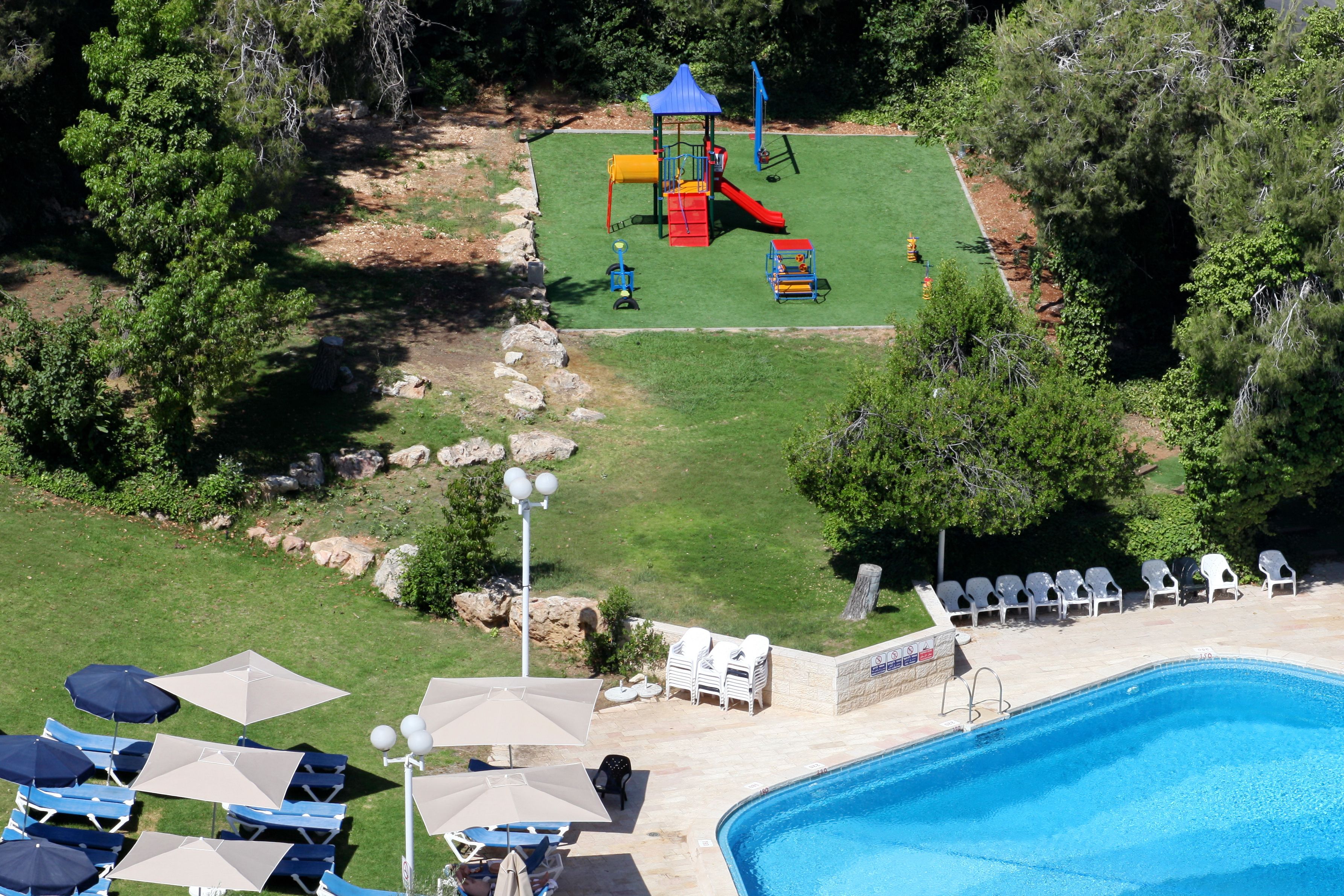 An aerial view of a backyard with a swimming pool, a play area with a slide, and lounge chairs.