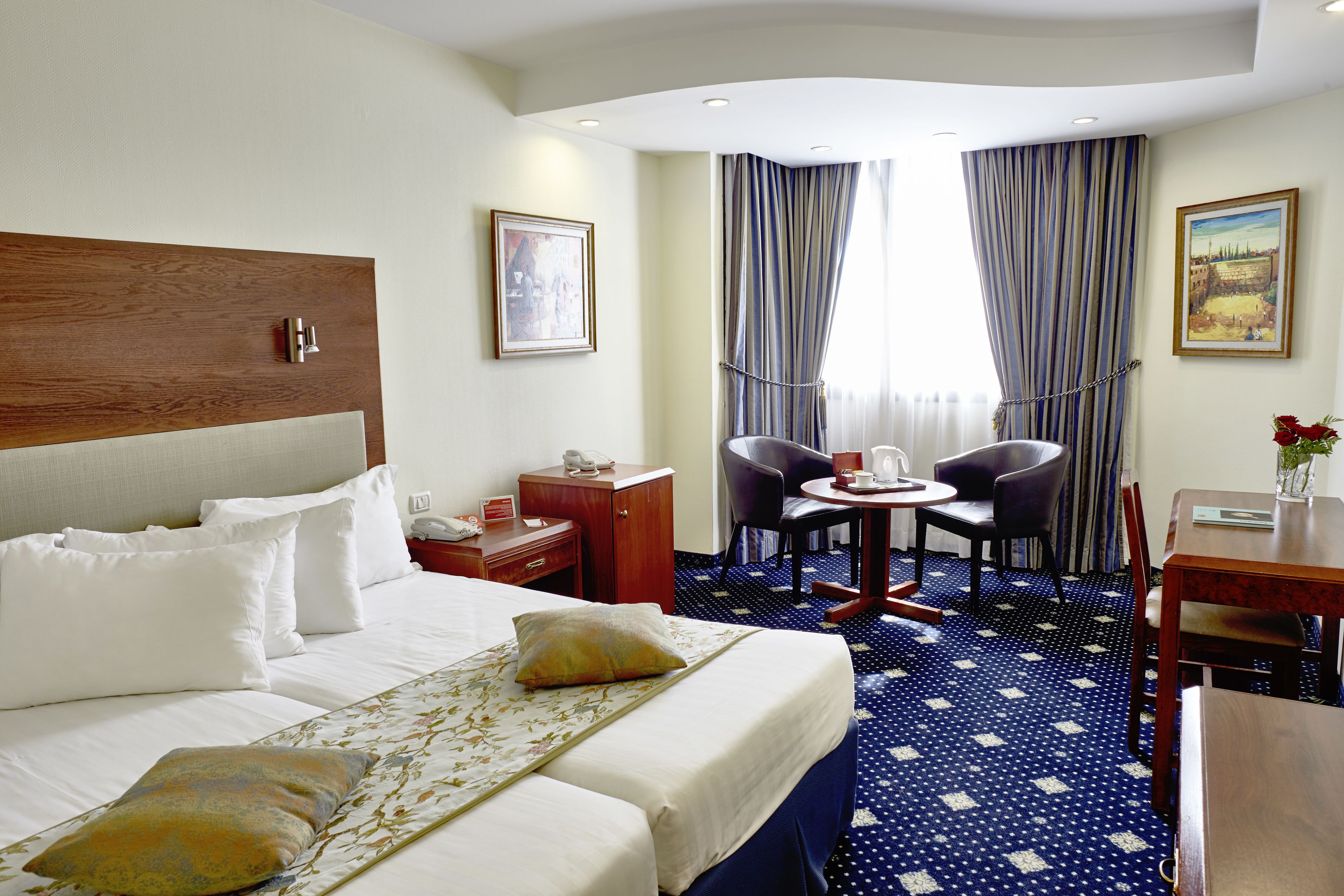 Una habitación de hotel con una cama grande, dos mesitas de noche, un escritorio con una silla, una pequeña mesa con dos sillas y una ventana con cortinas.