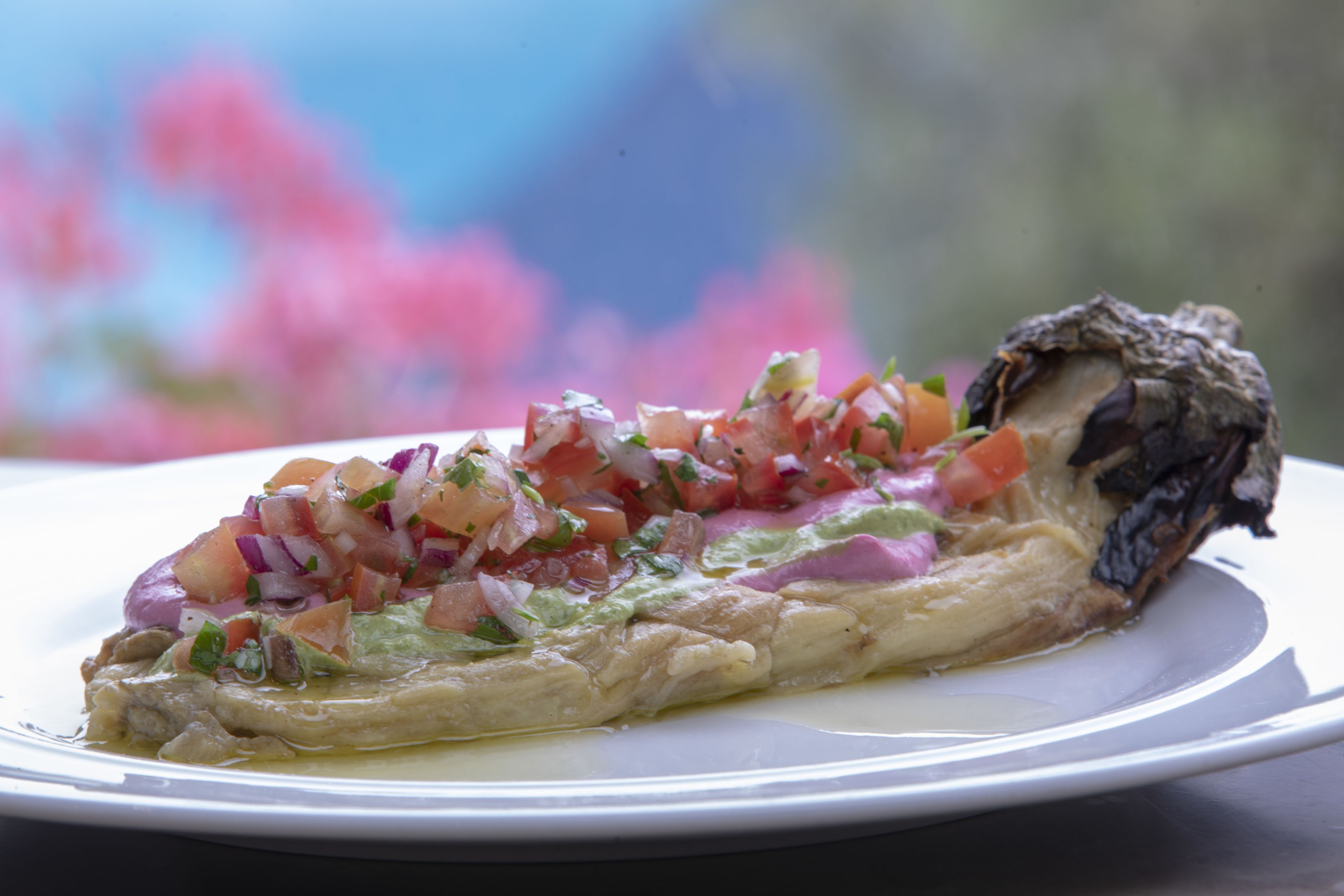 A plate with a slice of fish topped with a colorful salsa and a piece of bread.