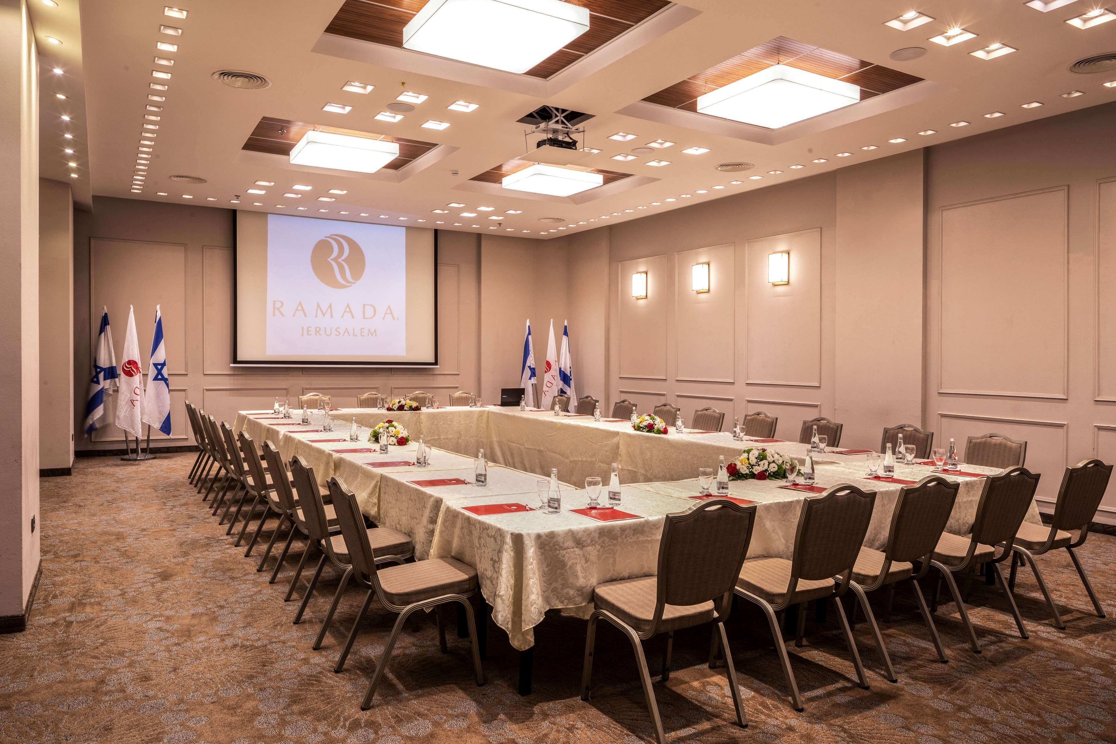 A conference room with a long table, chairs, and a projector screen displaying "RAMADA JERUSALEM".