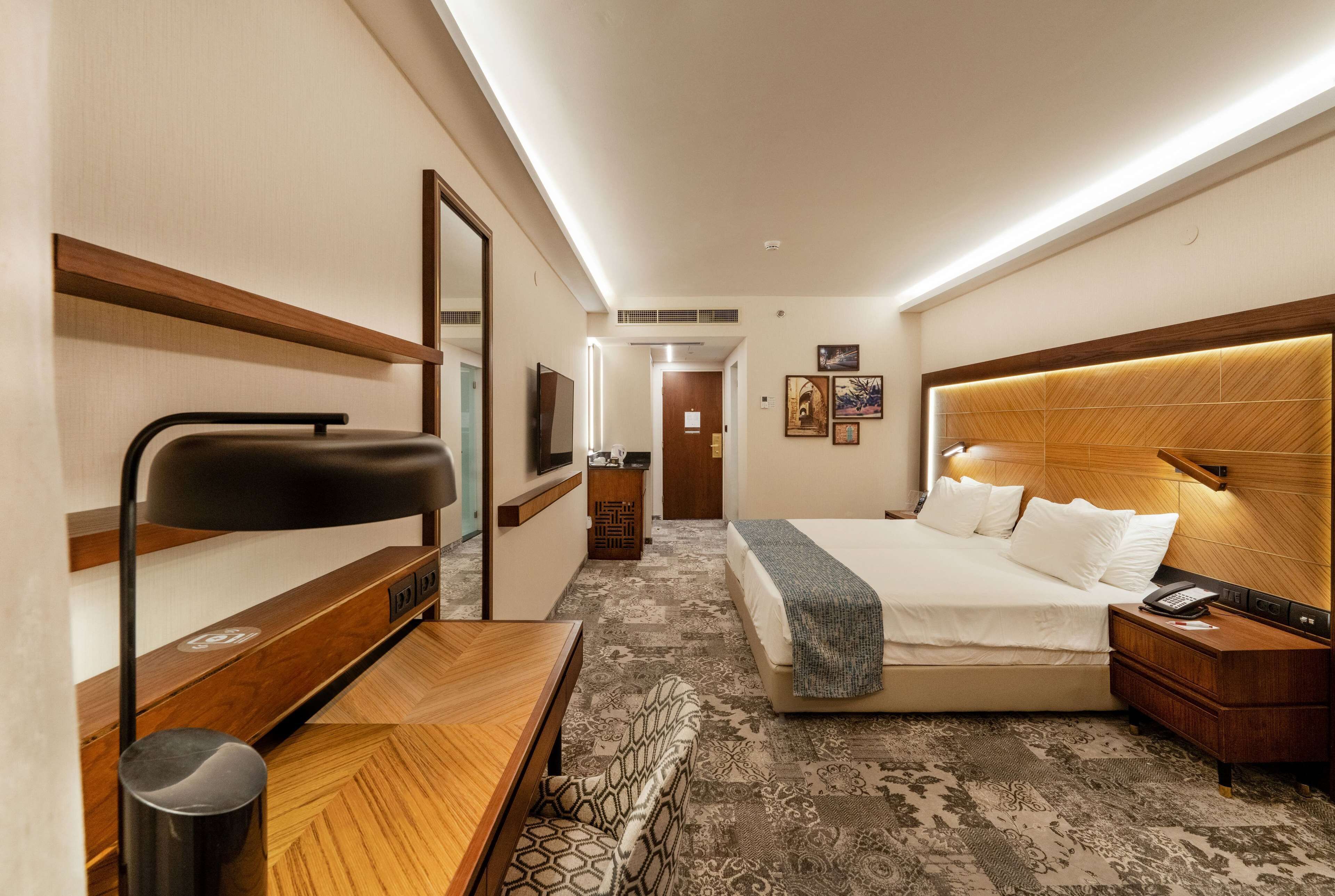 Une chambre d’hôtel comprenant un lit, une table de chevet, une lampe et un bureau avec une chaise.