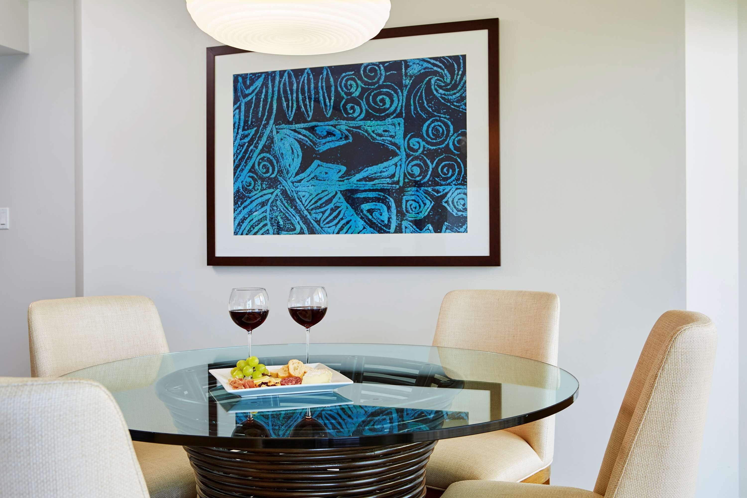 A dining area with a glass table, two chairs, a plate of food, and two glasses of red wine.