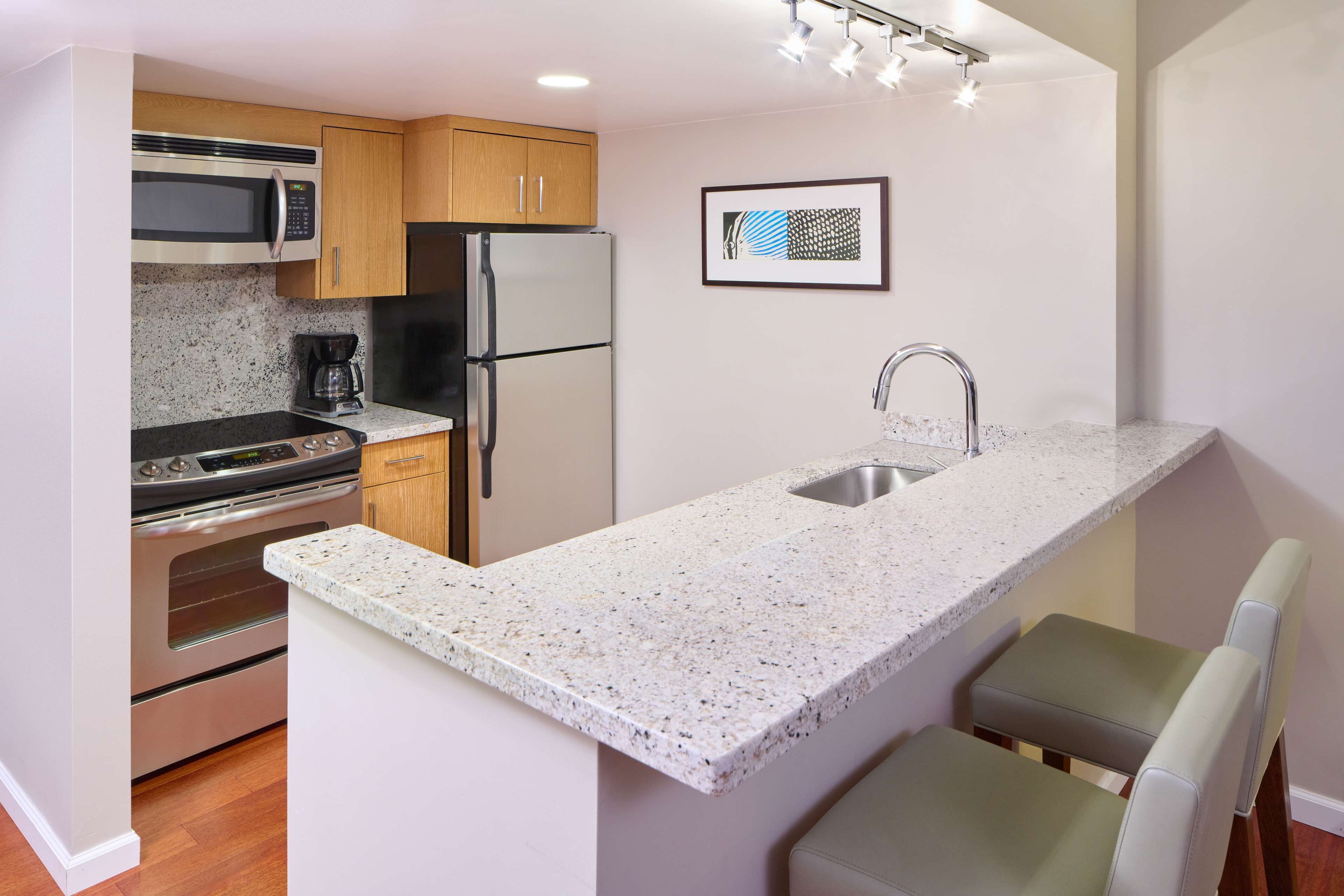 A modern kitchen with a granite countertop, stainless steel appliances, and a small dining area with a bench.