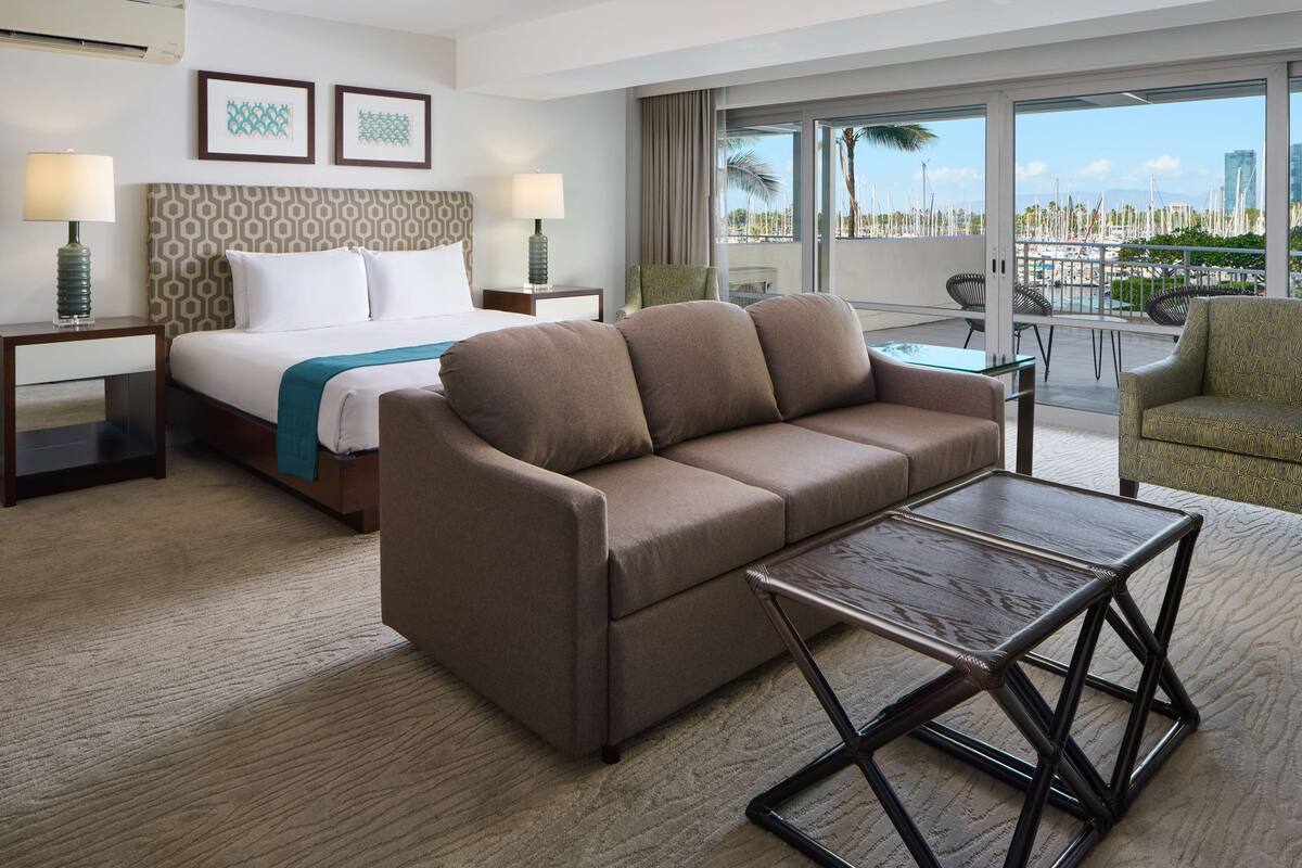 Une chambre d’hôtel comprenant un lit, un canapé, une petite table et un balcon avec vue sur le port de plaisance.