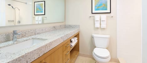 A modern bathroom with a granite countertop sink, wooden cabinets, a white toilet, and a framed picture on the wall.