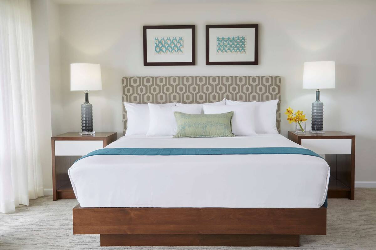 A hotel room with a large bed, two nightstands, a patterned headboard, and two framed pictures on the wall.