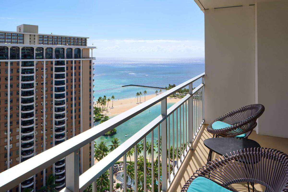 A balcony with wicker chairs and a view of a beach and ocean.