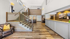 A spacious hallway with a wooden floor, a leather sofa, a staircase with a wooden railing, and a reception desk with a counter. - Best Western Inn At The Rogue (Grants Pass)