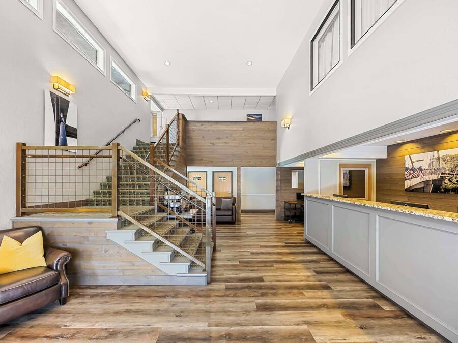 A spacious hallway with a wooden floor, a leather sofa, a staircase with a wooden railing, and a reception desk with a counter.
