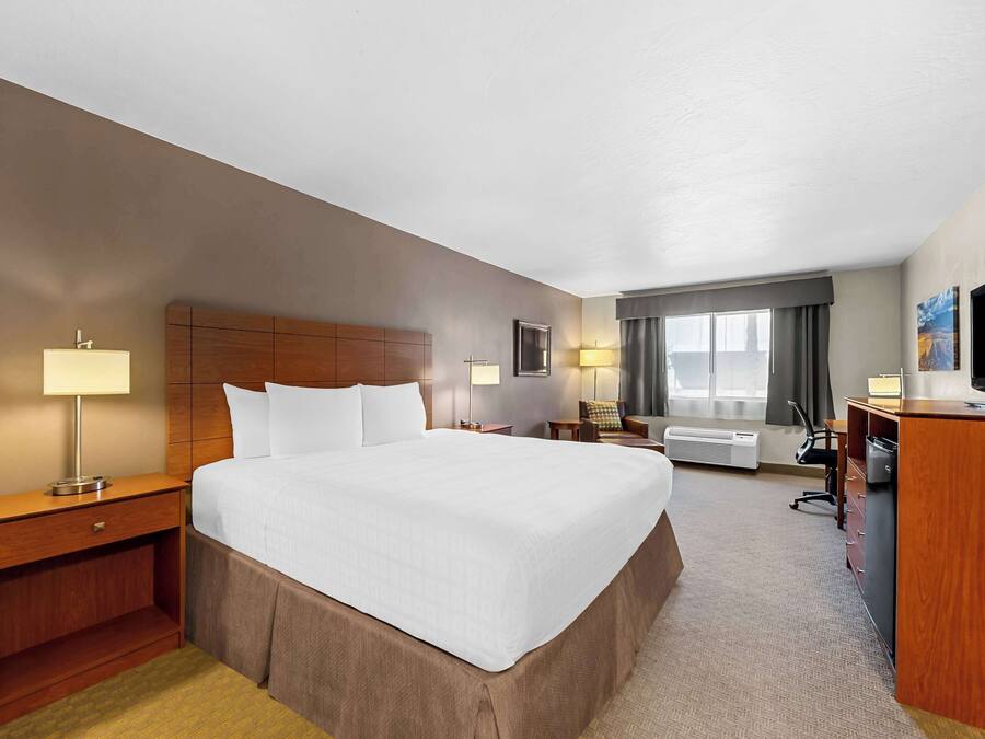 Ein Hotelzimmer mit einem großen Bett, einem Schreibtisch, einem Sessel, einem Fernseher und einem Fenster mit Vorhängen.