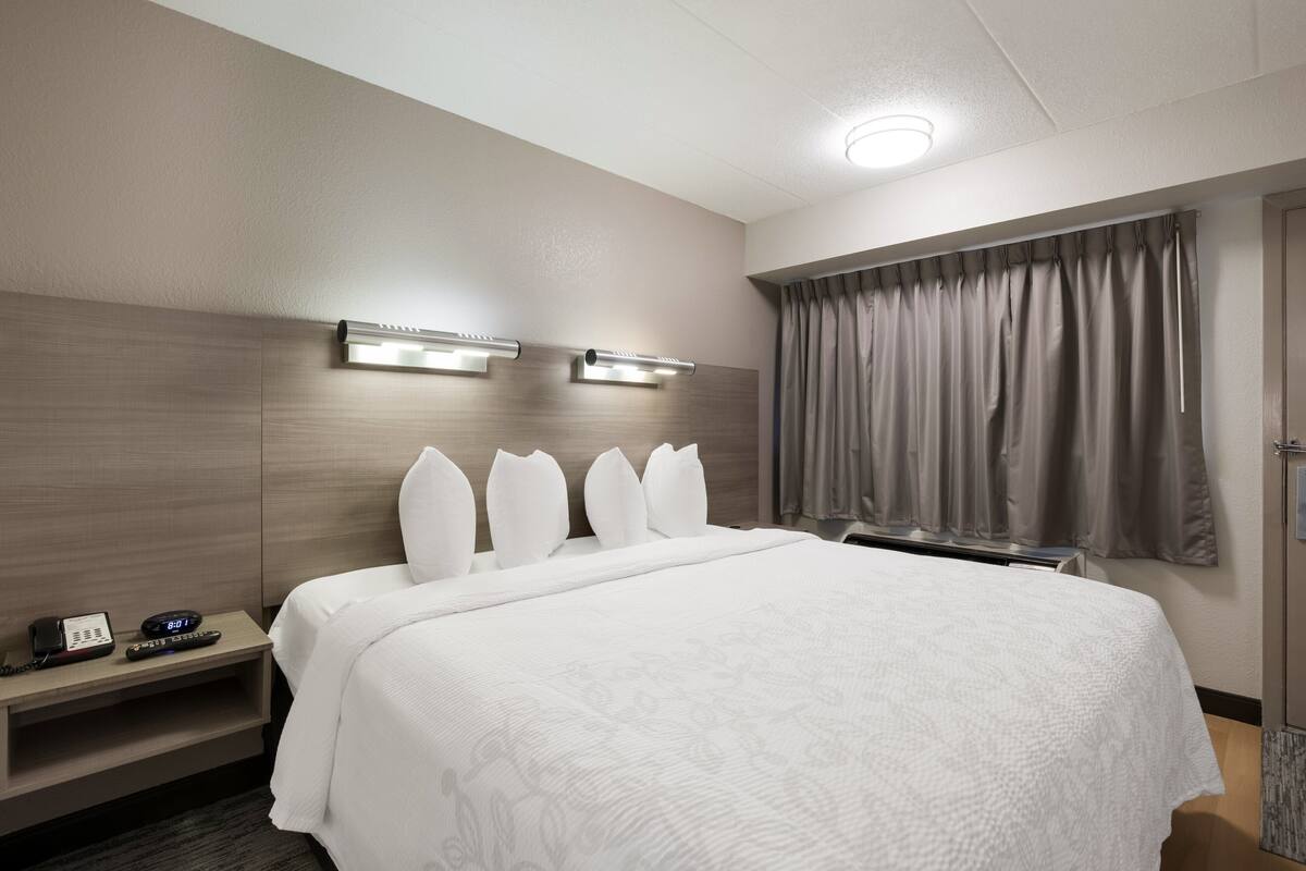 A hotel room with a large bed, a bedside table with a phone and remote control, and a window with curtains.