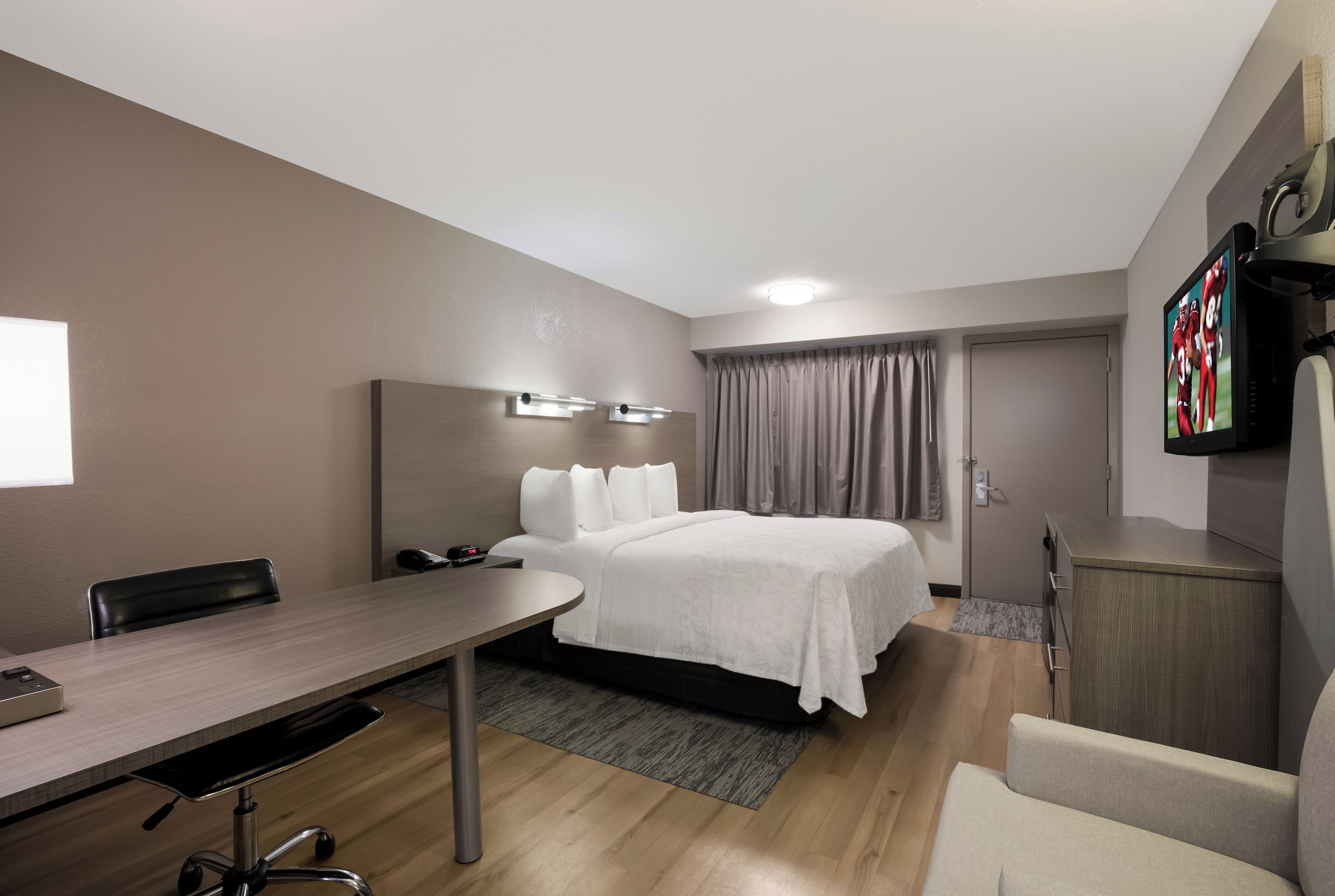 A hotel room with a bed, a desk, a chair, a TV, and a wardrobe.