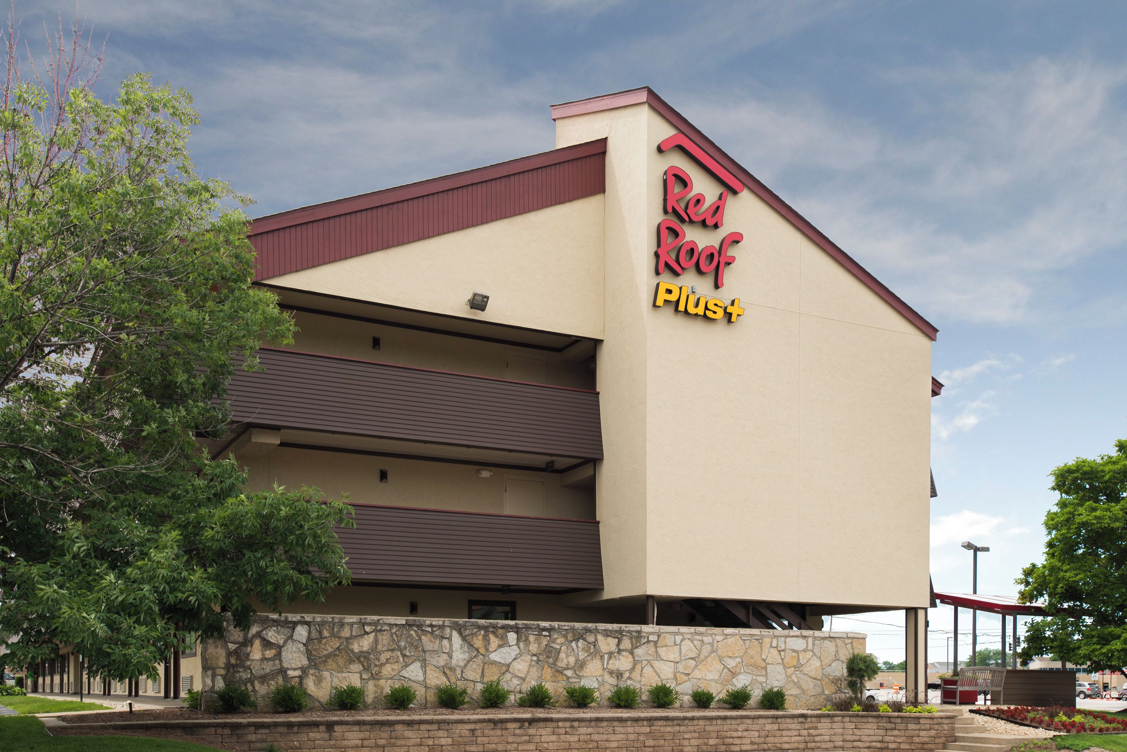 A Red Roof Plus hotel with a two-story structure, stone facade, and a parking lot in the foreground.