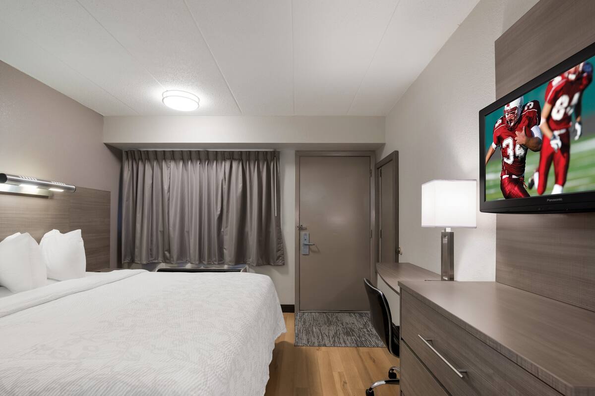 A hotel room with a bed, a desk, a television, and a door.