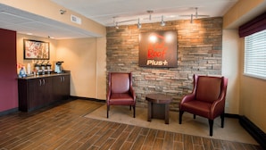 A reception area with a stone wall, two leather chairs, a coffee station, and a sign reading 'Red Rock Plus'. - Red Roof Inn PLUS+ Chicago - Naperville (Naperville)