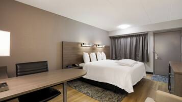 A hotel room with a bed, bedside table, desk, chair, and a wardrobe.