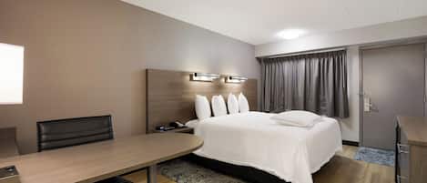 A hotel room with a bed, bedside table, desk, chair, and a wardrobe.