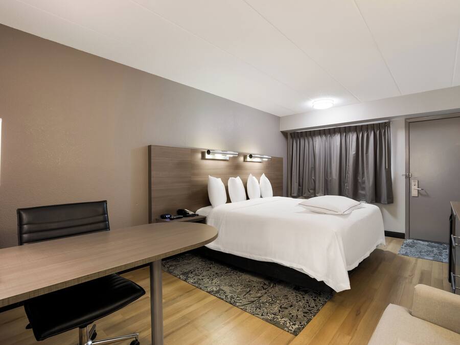 A hotel room with a bed, bedside table, desk, chair, and a wardrobe.