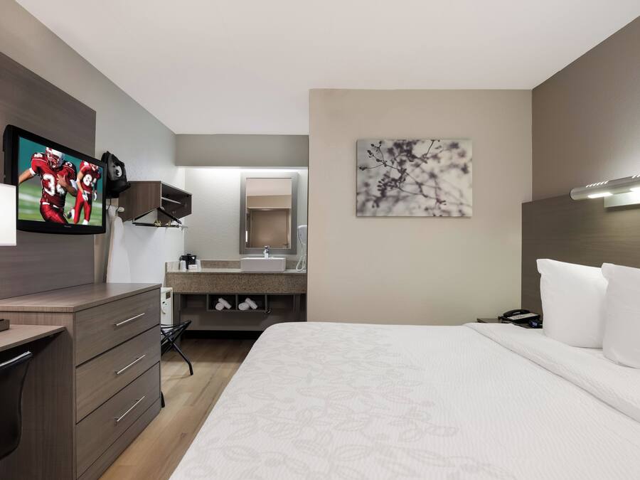 A hotel room with a bed, a desk, a television, a bathroom, and a painting on the wall.