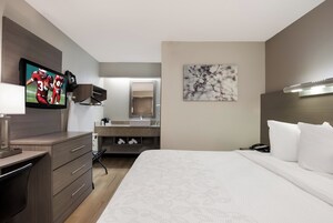 Habitación de hotel con cama, escritorio, televisión, baño y un cuadro en la pared.