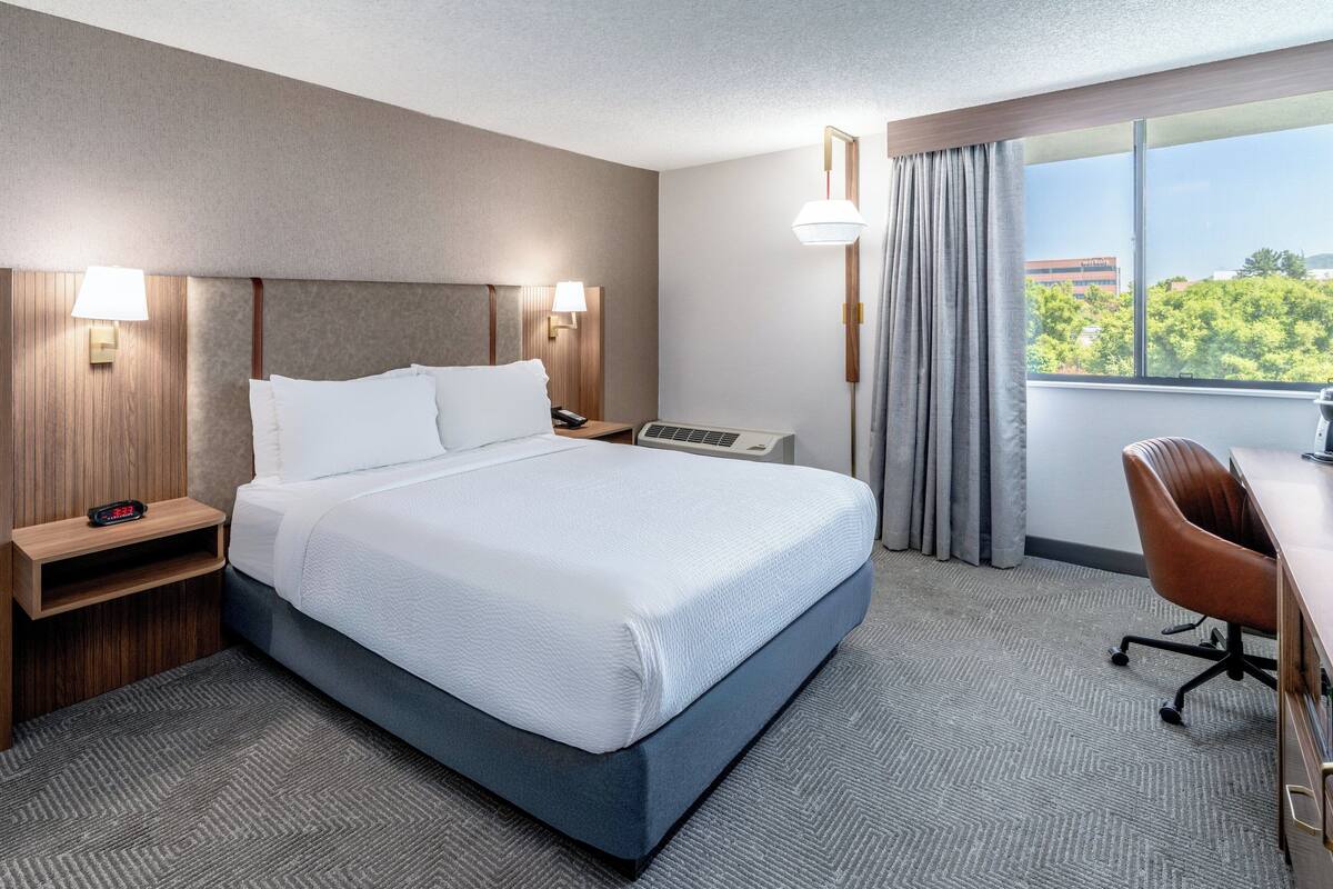A hotel room with a bed, bedside tables, a desk, and a chair.