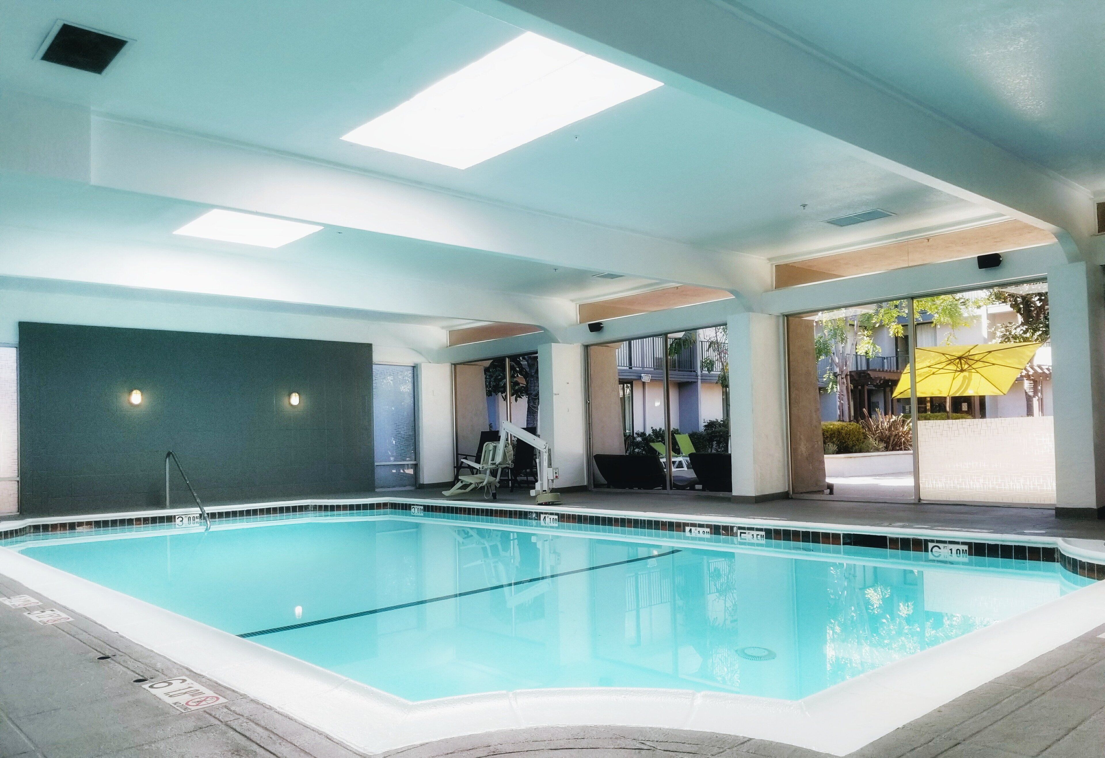 Una piscina interior con agua cristalina, un trampolín y una zona de estar con sillas.