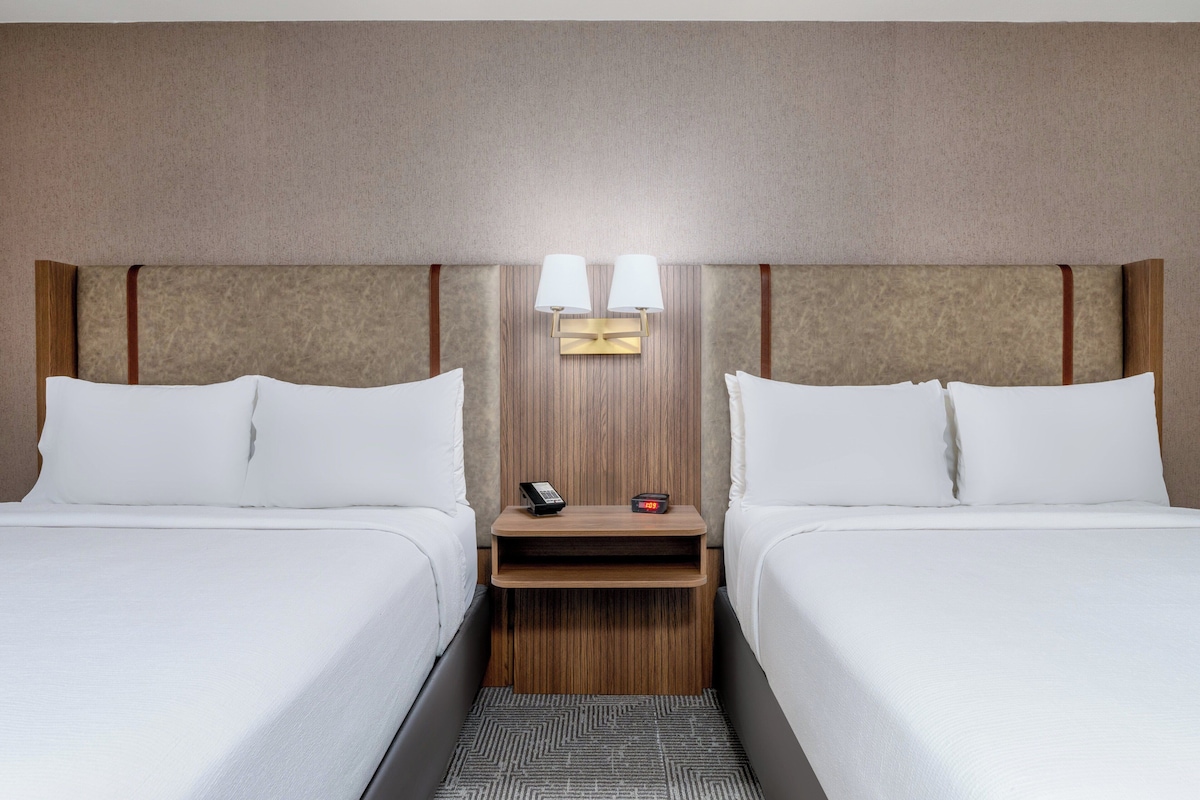 Ett hotellrum med två sängar, ett nattduksbord med en telefon och en väckarklocka samt en vägglampa.