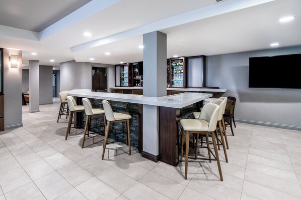 A modern kitchen with a central island, bar stools, and a built-in bar area with shelves of bottles.