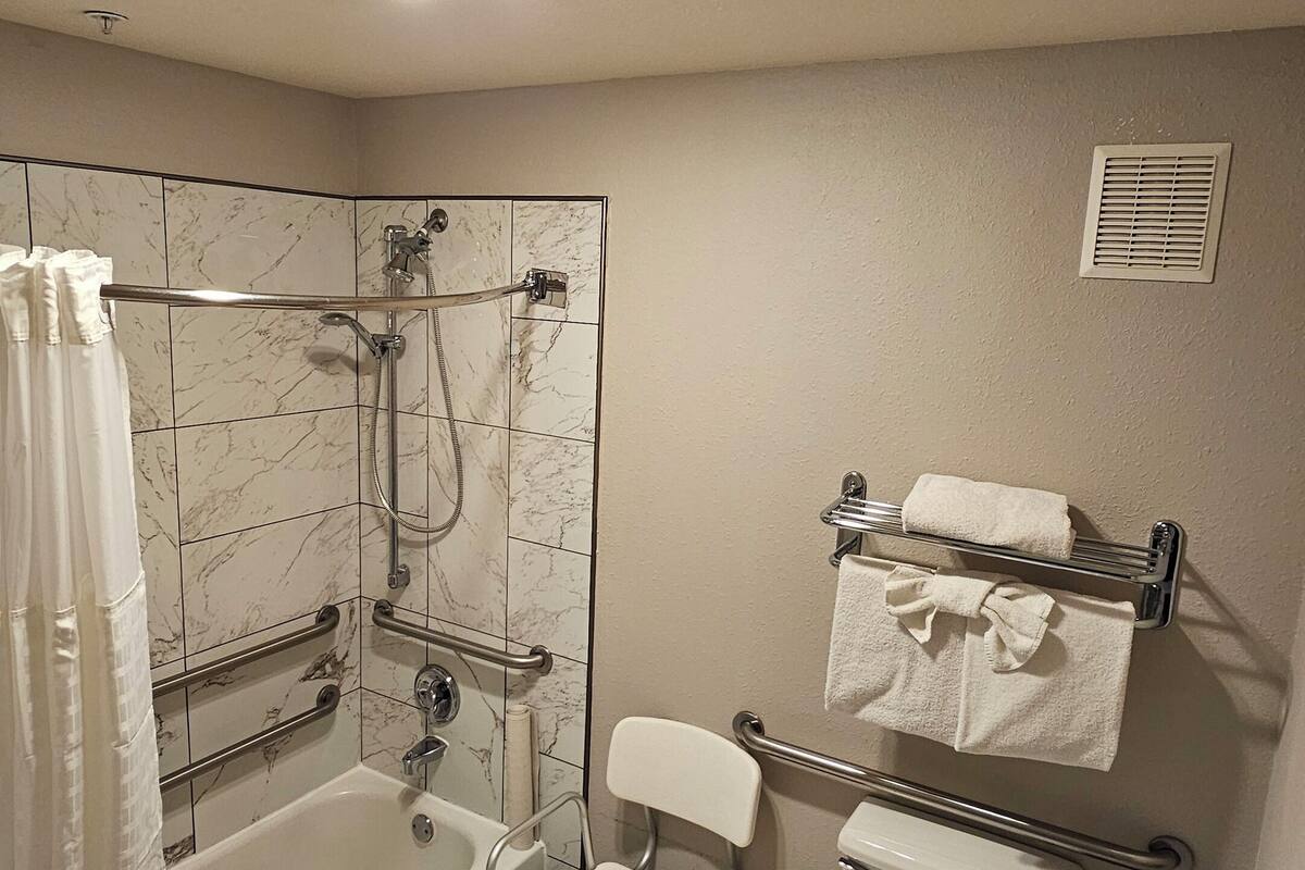 A bathroom with a bathtub, shower, toilet, and a grab bar.
