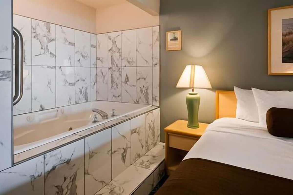 A hotel room with a marble bathroom, a bed with white and brown bedding, a green lamp, and a framed picture on the wall.