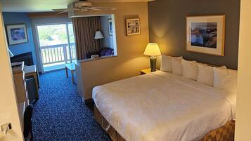 A hotel room with a large bed, a desk, a chair, a lamp, and a view of the outdoors.