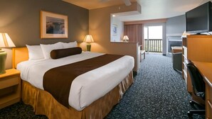 A hotel room with a large bed, a desk, a chair, a television, and a balcony with a view. - Lighthouse Suites Inn (Ocean Shores)