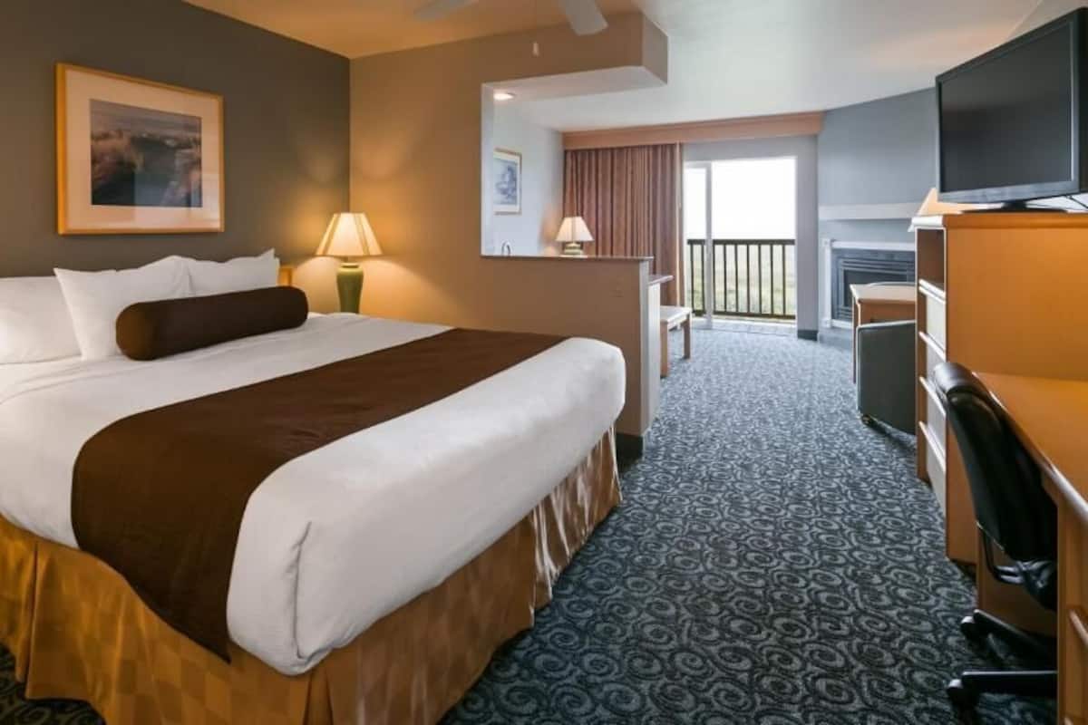 A hotel room with a large bed, a desk, a chair, a television, and a balcony with a view.