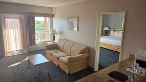 A hotel room with a sofa, a small table, a mirror, a bed, and a bathroom. - Lighthouse Suites Inn (Ocean Shores)