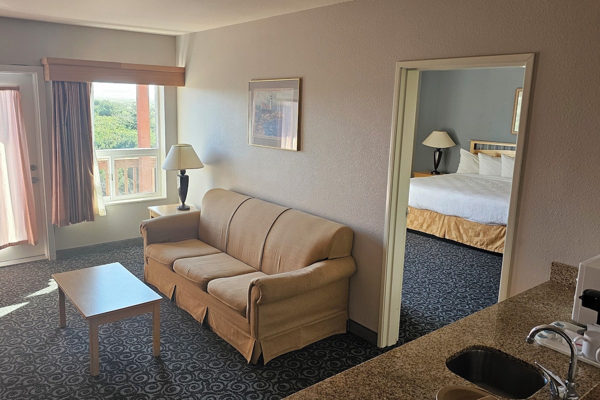 A hotel room with a sofa, a small table, a mirror, a bed, and a bathroom.