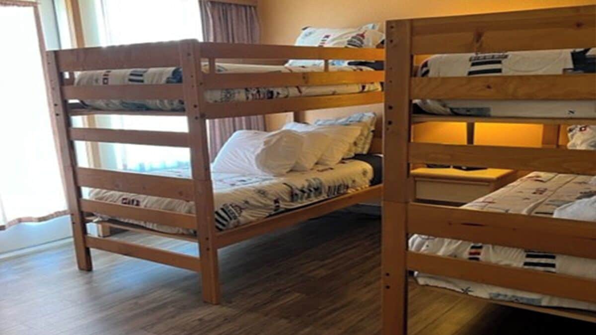 Een slaapkamer met stapelbedden, houten frames en witte beddengoed.