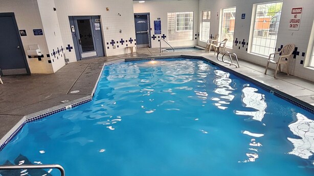 An indoor swimming pool with clear water, tiled walls, and a lifeguard chair. - Lighthouse Suites Inn (Ocean Shores)
