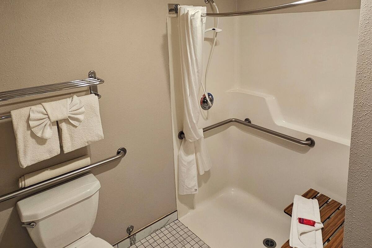 A small, clean bathroom with a toilet, a shower with a grab bar, and a bench.