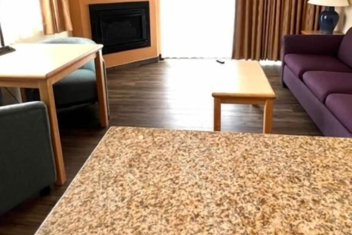 A hotel room with a large bed, a small table, a sofa, a fireplace, and a window with curtains.