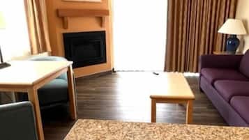 A hotel room with a large bed, a small table, a sofa, a fireplace, and a window with curtains.