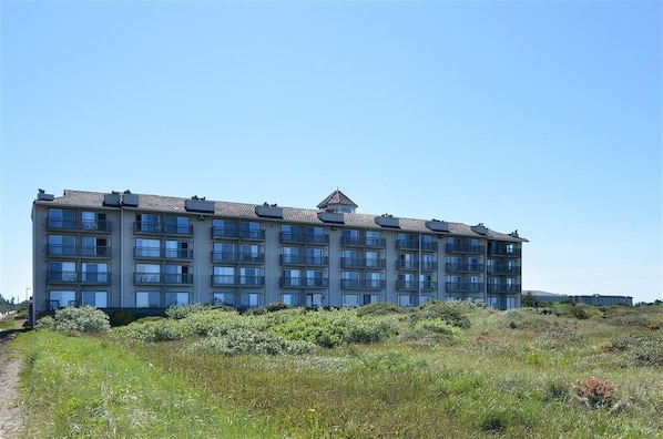 A multi-story building with a flat roof, several balconies, and a pathway leading to the entrance.